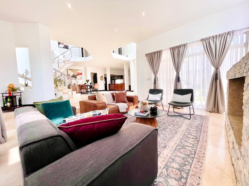 Spacious open-plan living area featuring a stone-clad fireplace, tiled flooring, and a grand staircase, seamlessly connecting to the dining space and outdoor access.