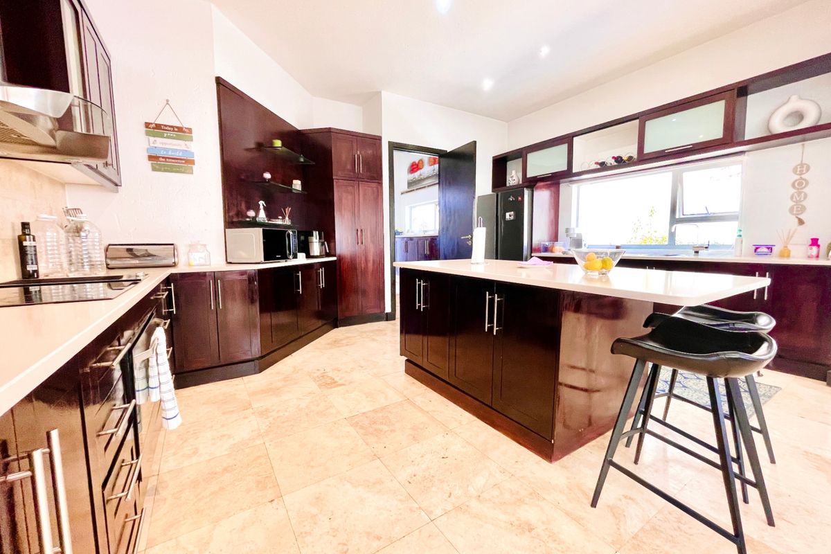 Spacious kitchen featuring dark wood cabinetry, a central island with stone countertops, stone flooring, and integrated appliances.