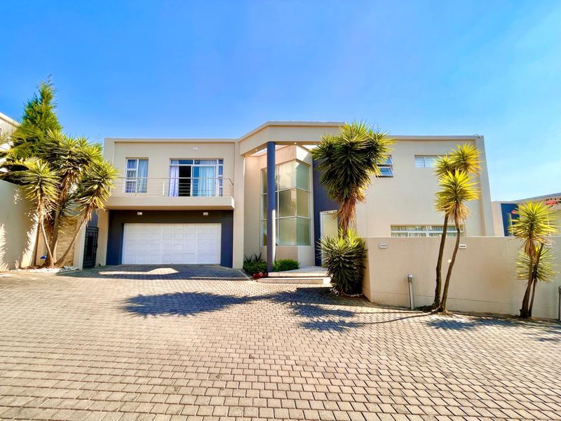 Modern double-storey residence featuring a paved driveway, double garage, and an upper-level balcony with stainless steel balustrades.