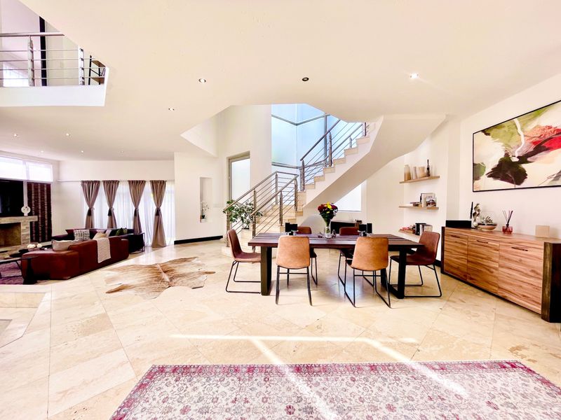 Spacious open-plan living and dining area featuring a grand staircase with stainless steel balustrades, stone flooring, and modern recessed lighting.
