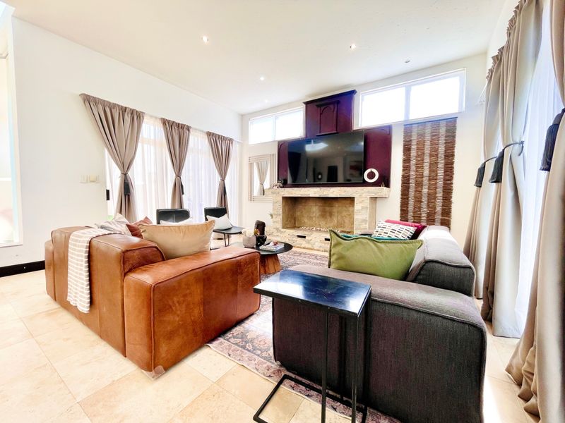 Spacious living room featuring a prominent stone fireplace, tiled flooring, and high ceilings with clerestory windows providing ample natural light.