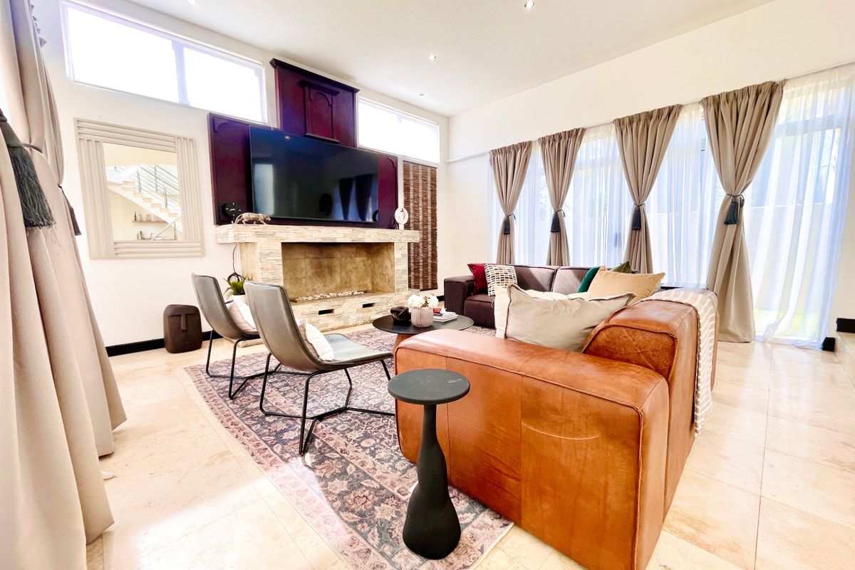 Spacious living room featuring a prominent stone fireplace, high ceilings with clerestory windows, and polished tile flooring, creating a bright and inviting atmosphere.