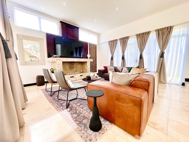 Spacious living room featuring a prominent stone fireplace, high ceilings with clerestory windows, and polished tile flooring, creating a bright and inviting atmosphere.