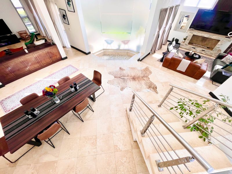 Spacious open-plan living and dining area featuring travertine flooring, a stone fireplace, and a modern staircase with stainless steel railings.