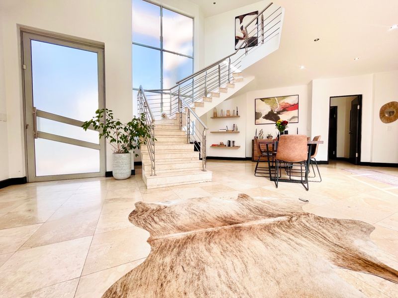 Spacious entrance hall featuring stone tile flooring, a striking floating staircase with stainless steel balustrades, and a large full-height window providing ample natural light.