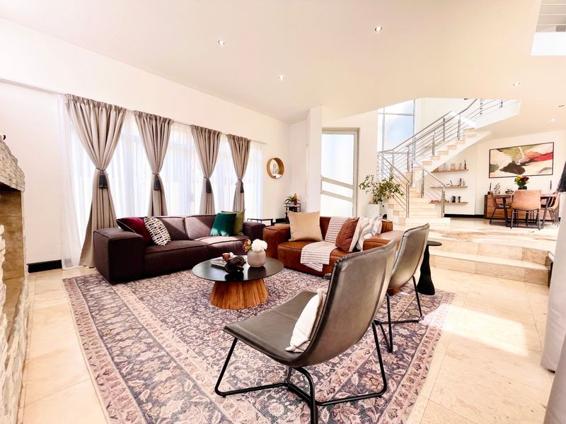 Spacious open-plan living area featuring stone flooring, a stone fireplace, and a modern staircase with a stainless steel balustrade.