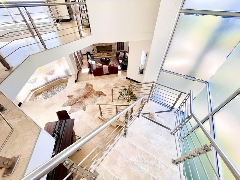 A grand double-volume entrance hall featuring a stone staircase with stainless steel balustrades, travertine flooring, and an open-plan view into the living area.