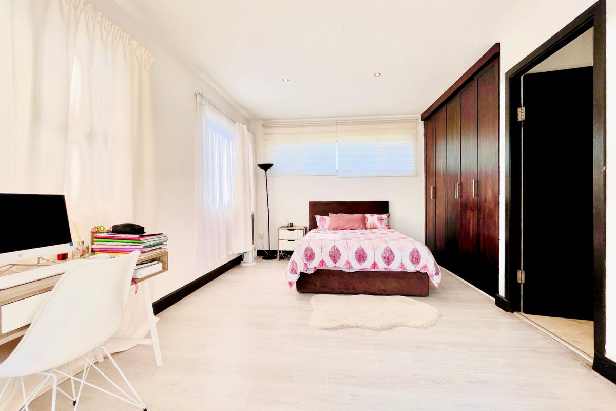 A well-maintained bedroom featuring light laminate flooring, recessed downlighting, and dark wood built-in cupboards providing ample storage space.