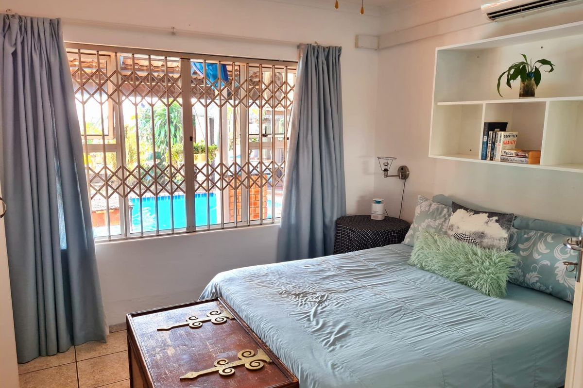 A bedroom featuring tiled flooring, built-in shelving, and a split-system air conditioner, with a security gate over the window overlooking the pool area.