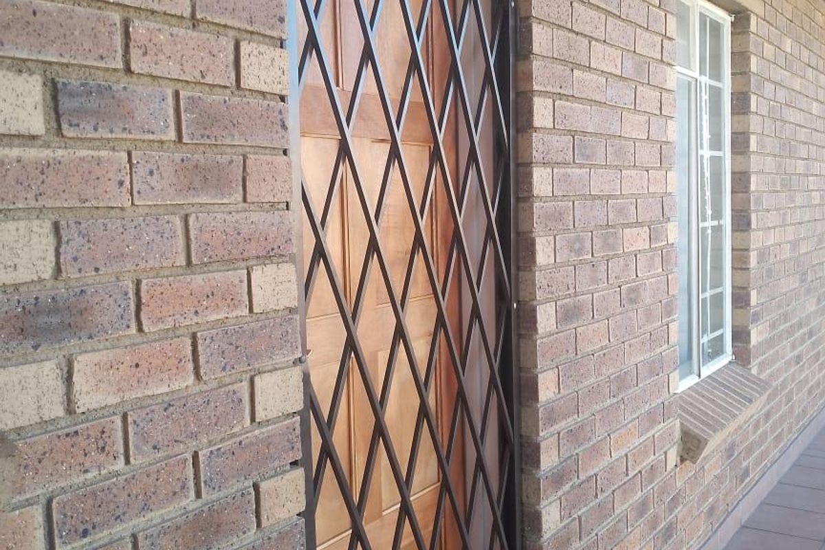 Exterior view of an apartment entrance featuring a brick facade, a timber door with a security gate, and a tiled walkway.