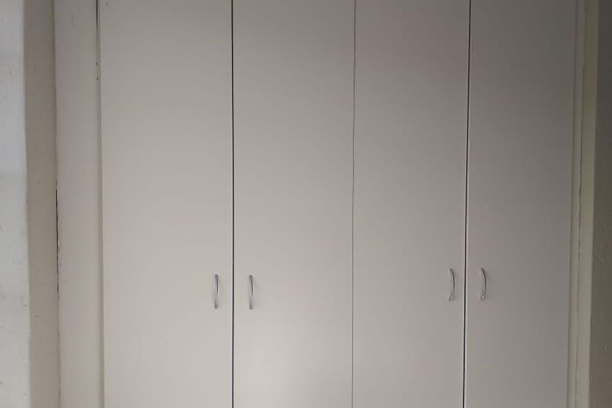 A bedroom featuring a full-height, white built-in wardrobe with modern handles.