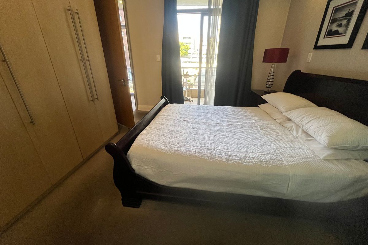 A well-lit bedroom featuring built-in cupboards and direct access to a private balcony through a sliding glass door.