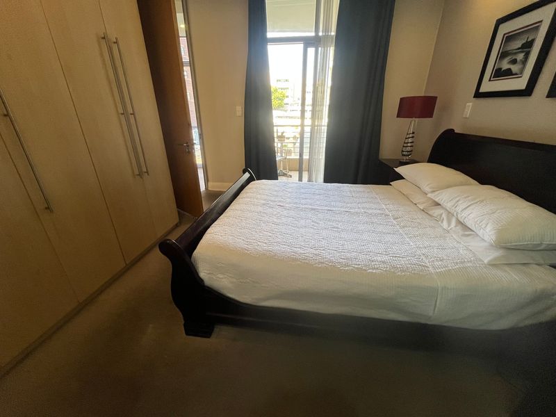 A well-lit bedroom featuring built-in cupboards and direct access to a private balcony through a sliding glass door.