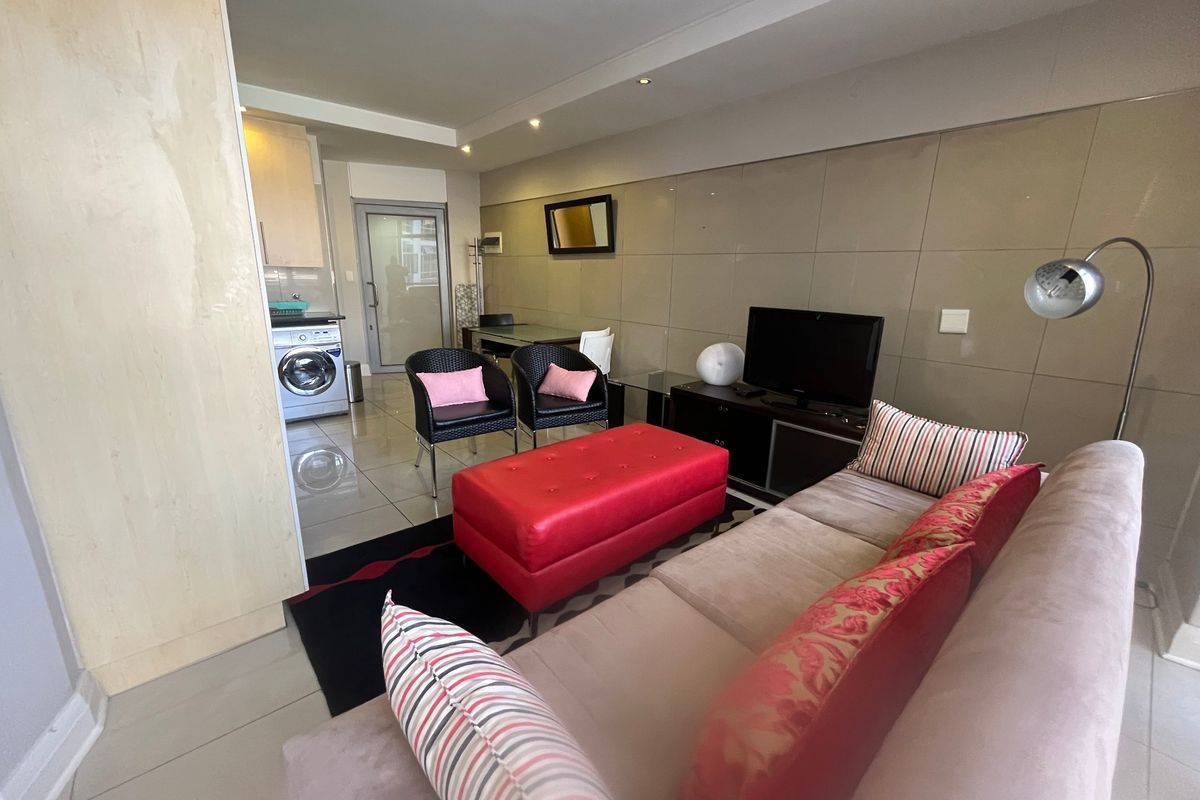 An open-plan living area featuring tiled flooring, recessed lighting, and a modern tiled feature wall, seamlessly incorporating a compact laundry space.