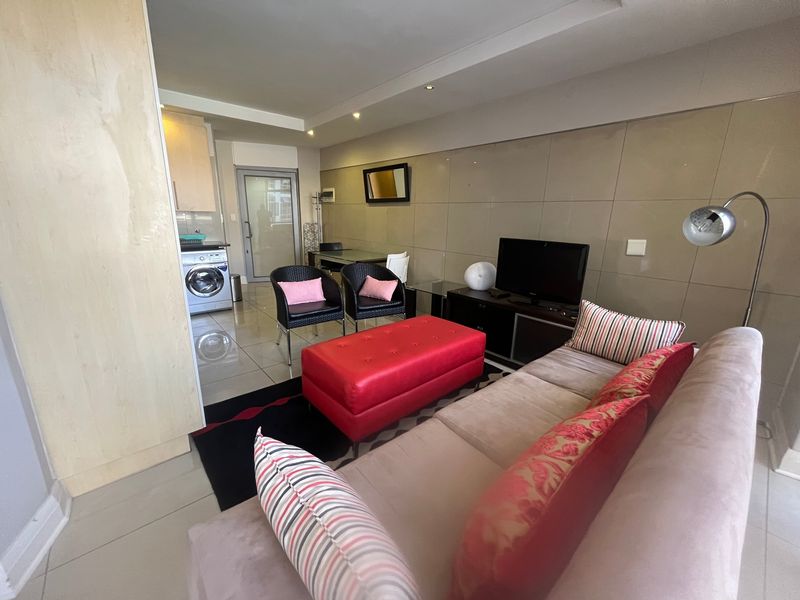 An open-plan living area featuring tiled flooring, recessed lighting, and a modern tiled feature wall, seamlessly incorporating a compact laundry space.