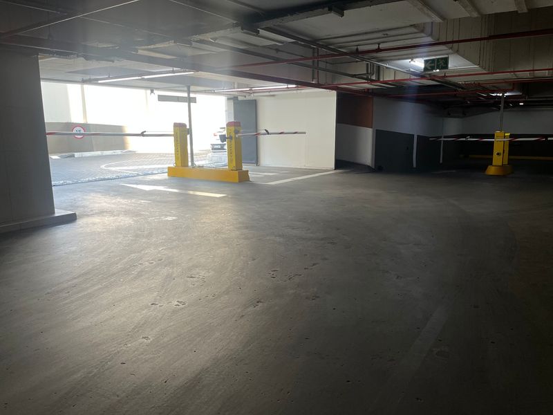 Underground parking garage area featuring concrete flooring, automated boom gate access, and exposed overhead fire safety infrastructure.