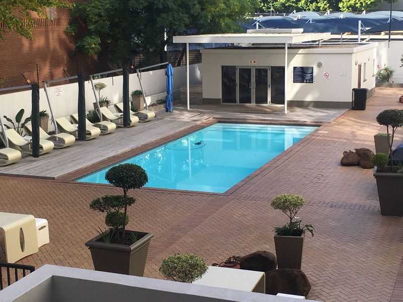 A well-maintained communal swimming pool area featuring paved surrounds, wooden decking, and a dedicated pool house facility.