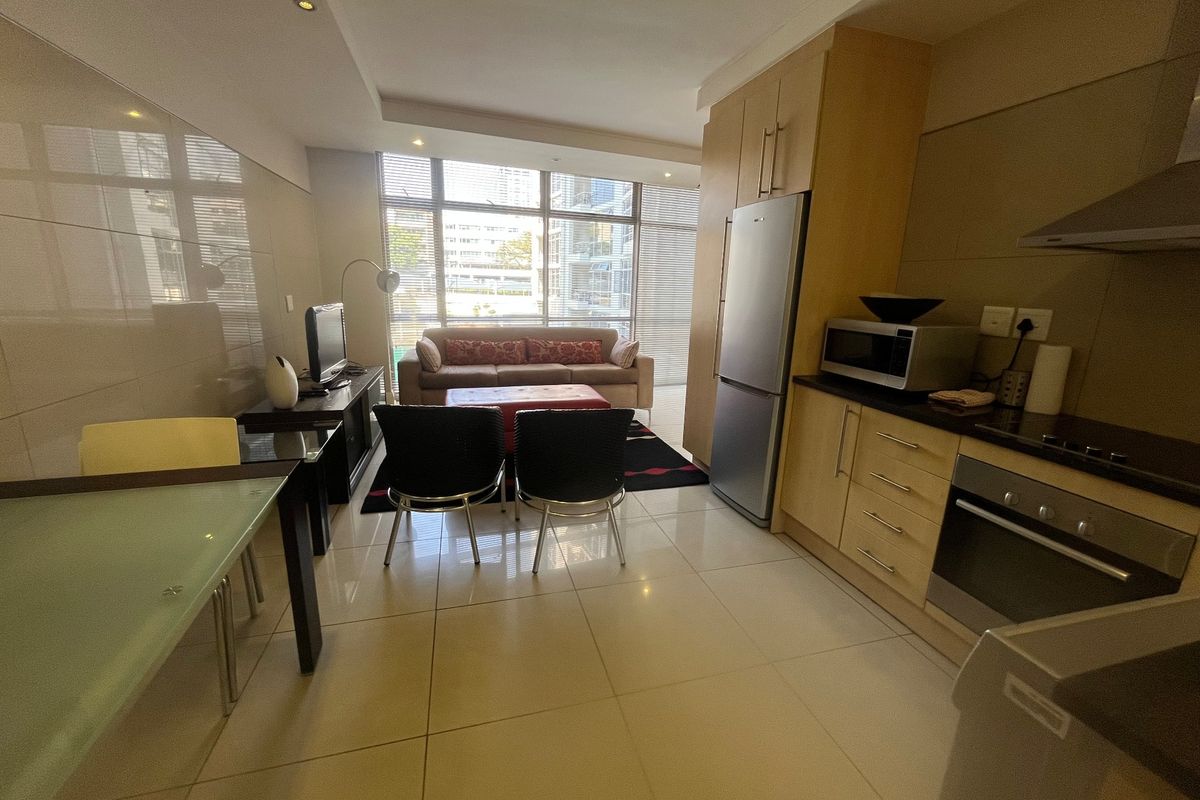 Open-plan living and kitchen area featuring tiled flooring, modern built-in cabinetry, integrated oven, and large windows providing ample natural light.