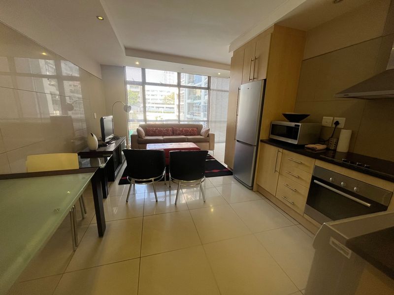 Open-plan living and kitchen area featuring tiled flooring, modern built-in cabinetry, integrated oven, and large windows providing ample natural light.
