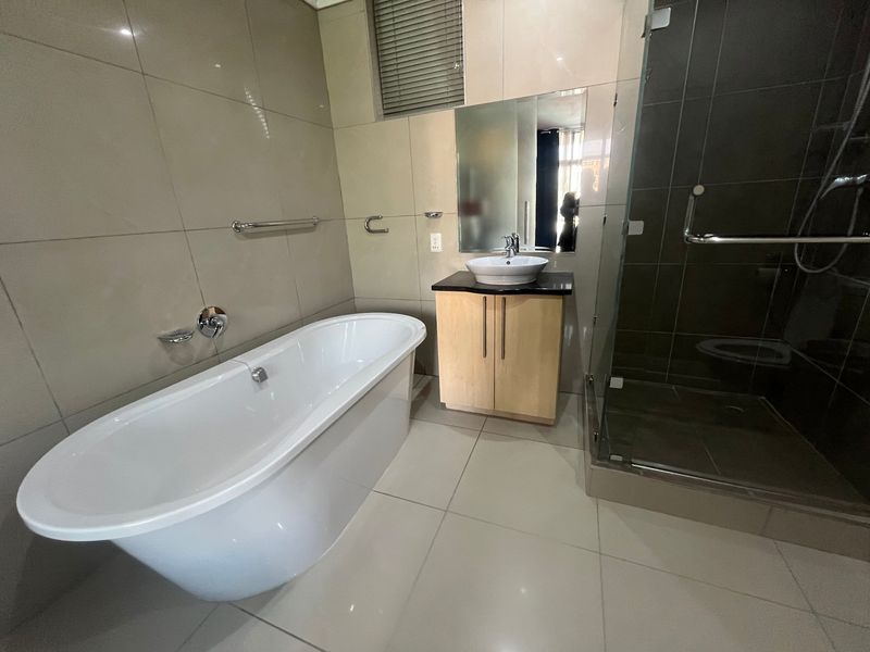 Modern bathroom featuring a freestanding bathtub, a glass-enclosed shower, and a vanity with a vessel sink, finished with neutral wall and floor tiles.