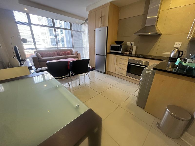 Modern open-plan apartment featuring a functional kitchen with built-in appliances, granite countertops, and bright living area with large windows.