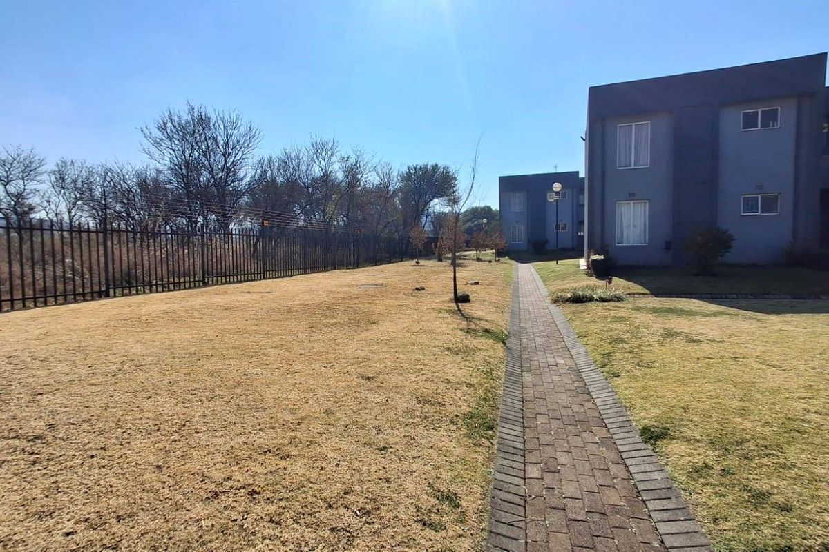 A view of the rear exterior area featuring a paved walkway, lawn, and perimeter fencing alongside the townhouse building facade.