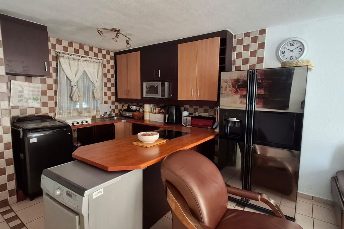 A functional kitchen featuring dark and wood-tone cabinetry, a laminate breakfast bar, and a distinctive checkered tile backsplash.