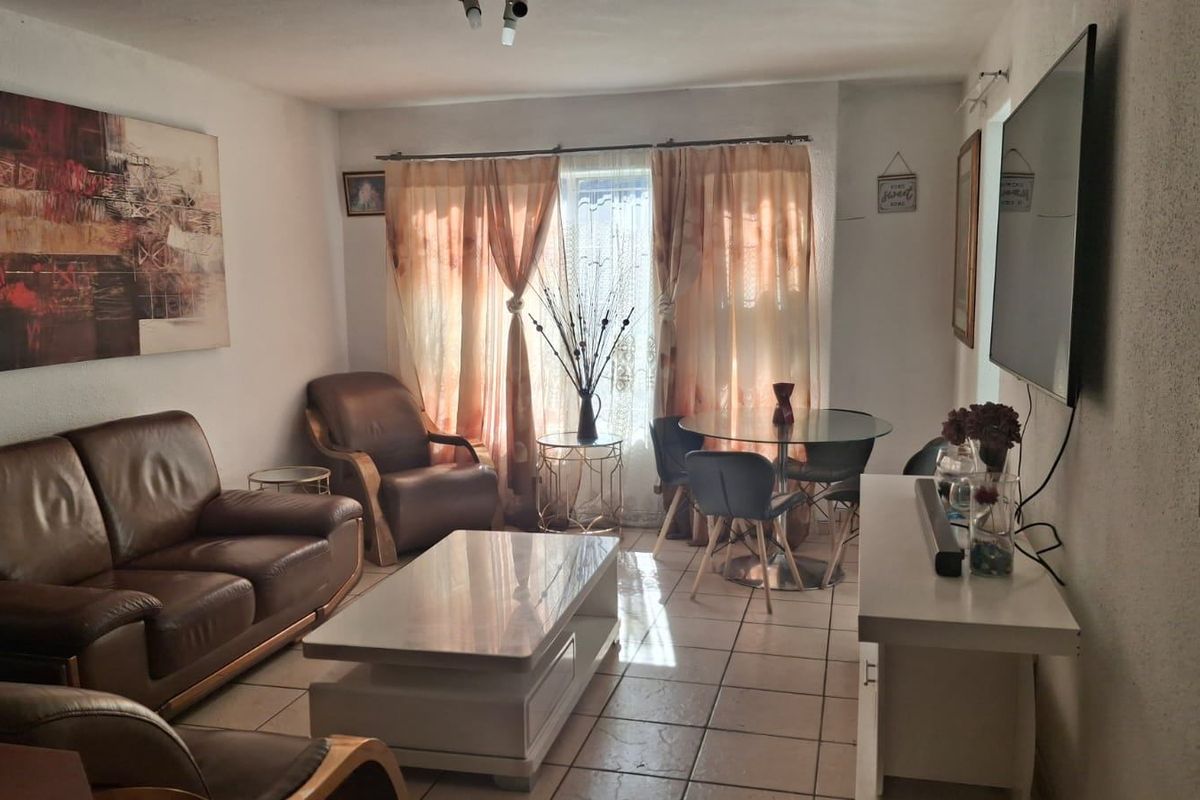 A living room area featuring tiled flooring and natural light through a window with curtain treatments.