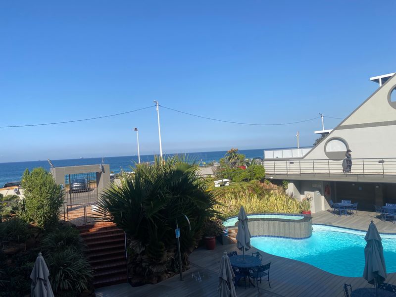 A well-maintained outdoor pool area featuring a swimming pool, wooden decking, and scenic ocean views, providing a relaxing communal space.