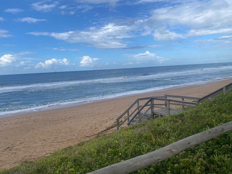 A scenic view of the sandy beach and ocean, featuring a wooden staircase providing direct access to the shoreline.