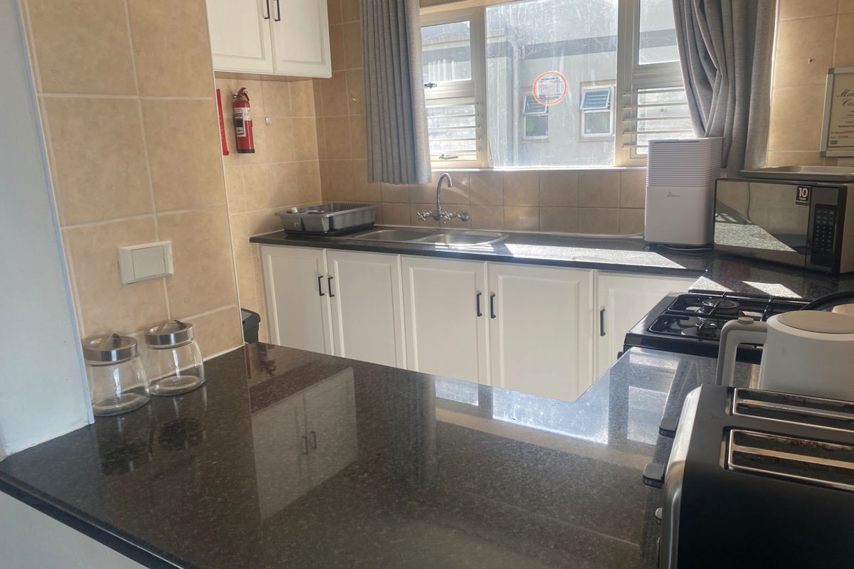 A functional kitchen featuring granite countertops, white cabinetry, tiled splashbacks, and a built-in gas hob with a stainless steel sink.