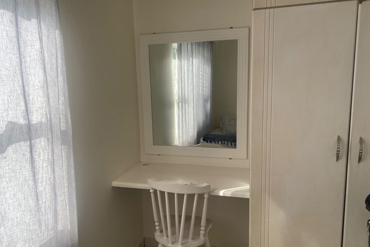 A bedroom featuring a built-in vanity with a wall-mounted mirror and a built-in wardrobe, finished with tiled flooring.