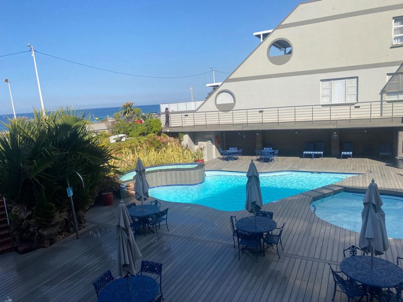 Outdoor pool area featuring a swimming pool, timber decking, and ocean views, providing a communal recreational space for the apartment complex.