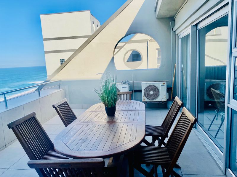 A spacious balcony featuring tiled flooring, a metal balustrade, and direct access to the interior through large sliding glass doors, offering ocean views.