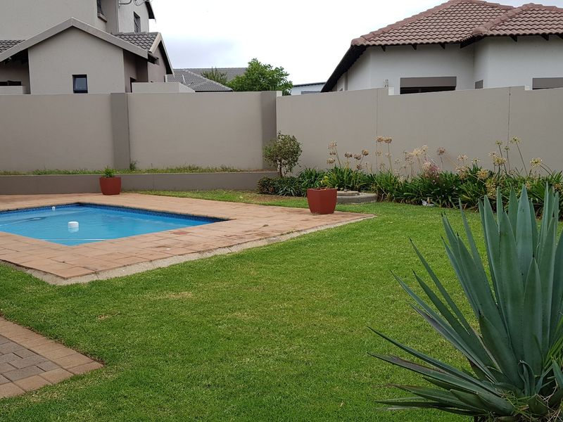 A private backyard featuring a swimming pool with paved surround, a well-maintained lawn, and high boundary walls for privacy.