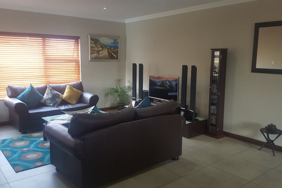 A comfortable living room featuring neutral tiled flooring, recessed downlighting, and large windows fitted with venetian blinds.