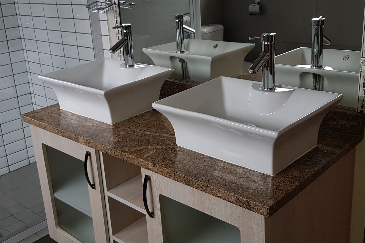 Modern bathroom featuring a double vanity with granite countertop, dual vessel sinks, chrome fixtures, and a tiled shower enclosure.