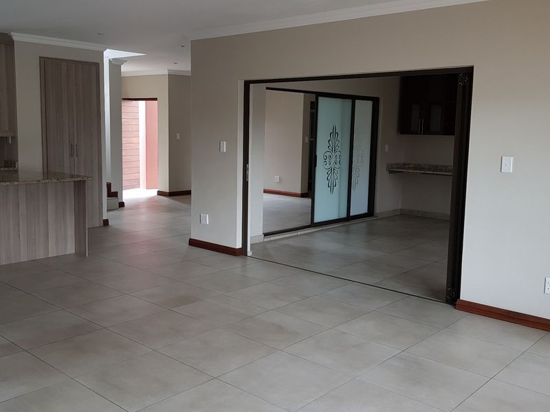 Spacious open-plan living area featuring neutral tiled flooring, modern kitchen cabinetry with granite countertops, and sliding glass doors leading to an adjacent room.