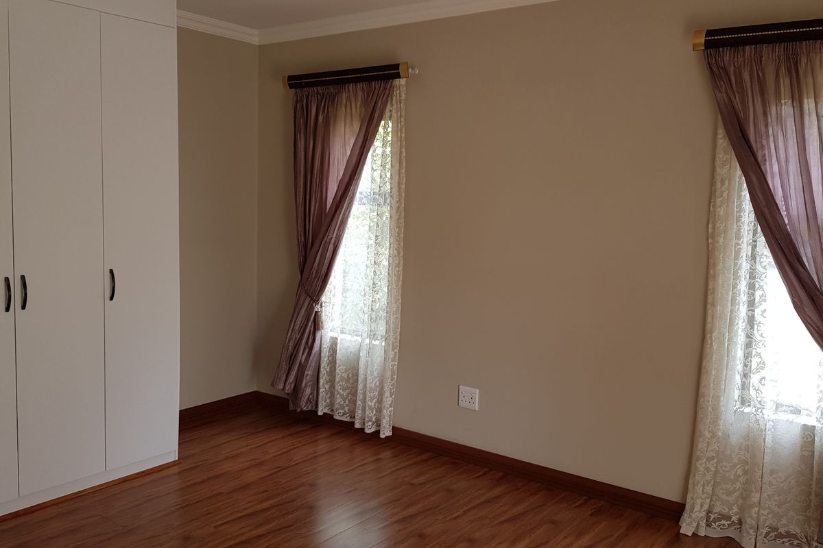 A bright, empty bedroom featuring laminate flooring, neutral walls, and built-in cupboards, offering a clean and versatile space ready for personalization.