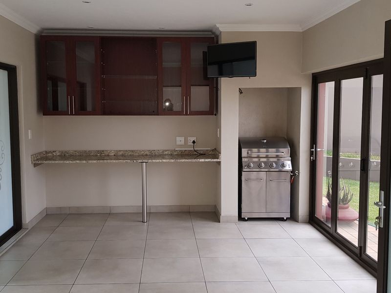 Covered patio area featuring built-in cabinetry, granite workspace, and a stainless steel built-in gas braai, with direct access to the garden through sliding doors.