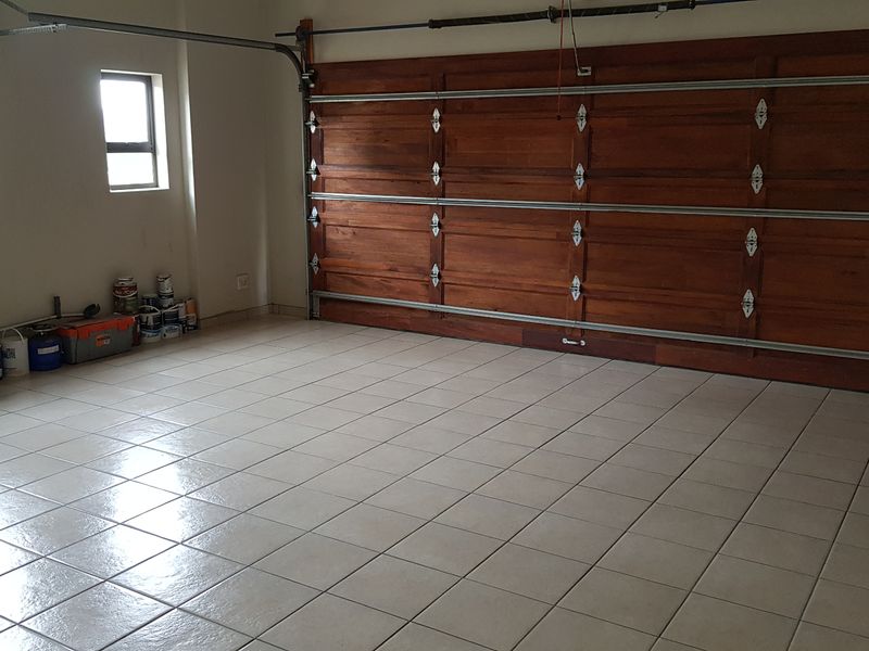A spacious, clean garage featuring tiled flooring and a large sectional timber garage door with an automated rail system.