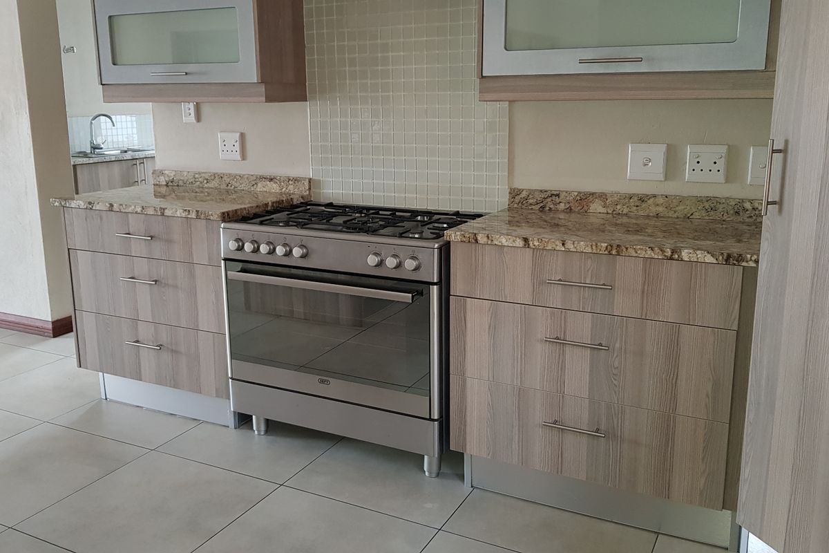 A clean, modern kitchen featuring granite countertops, wood-finish cabinetry, a gas stove, and tiled flooring, offering a functional and well-maintained cooking space.
