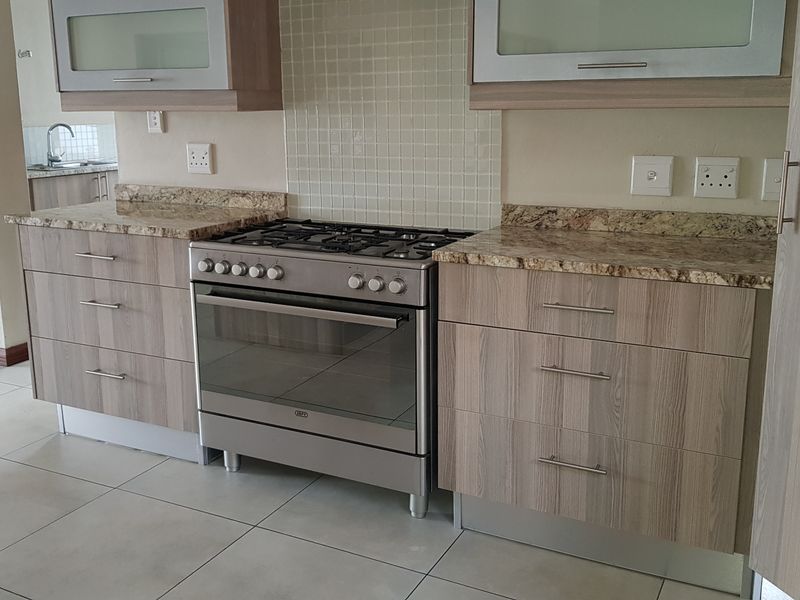 A clean, modern kitchen featuring granite countertops, wood-finish cabinetry, a gas stove, and tiled flooring, offering a functional and well-maintained cooking space.