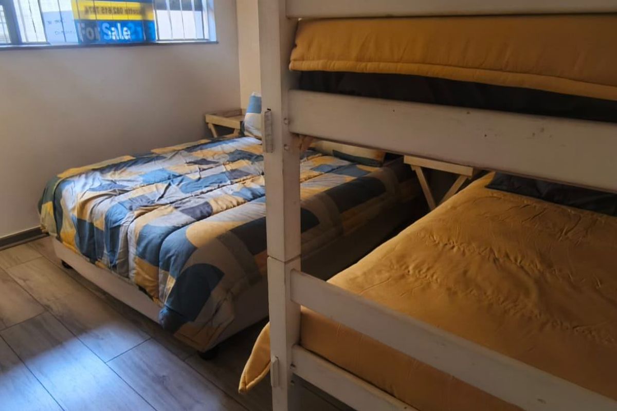 A bedroom featuring laminate flooring and a window with security bars, currently configured with multiple beds.