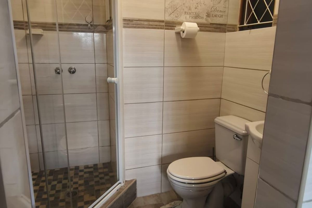 A functional bathroom featuring a corner shower enclosure, toilet, and pedestal basin with neutral wall and floor tiling.