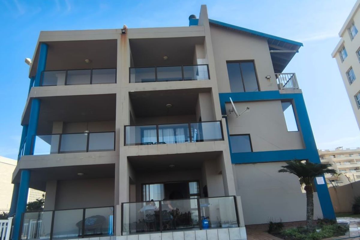 Rear elevation of a multi-story apartment building featuring stacked balconies with glass balustrades and paved ground-level patio space.