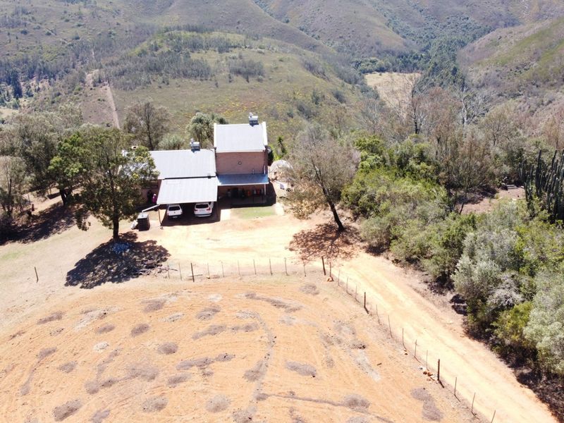 Aerial view of a rural farm property featuring a main dwelling with a metal roof, covered carport, and expansive surrounding landscape.