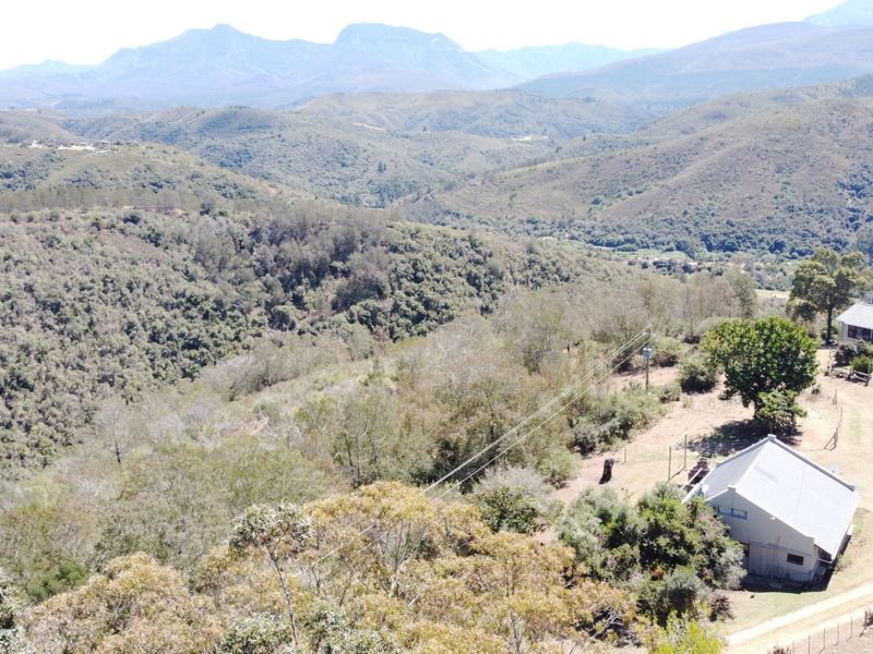 Aerial view of the farm property showcasing the main dwelling, outbuildings, and expansive surrounding mountain landscape.