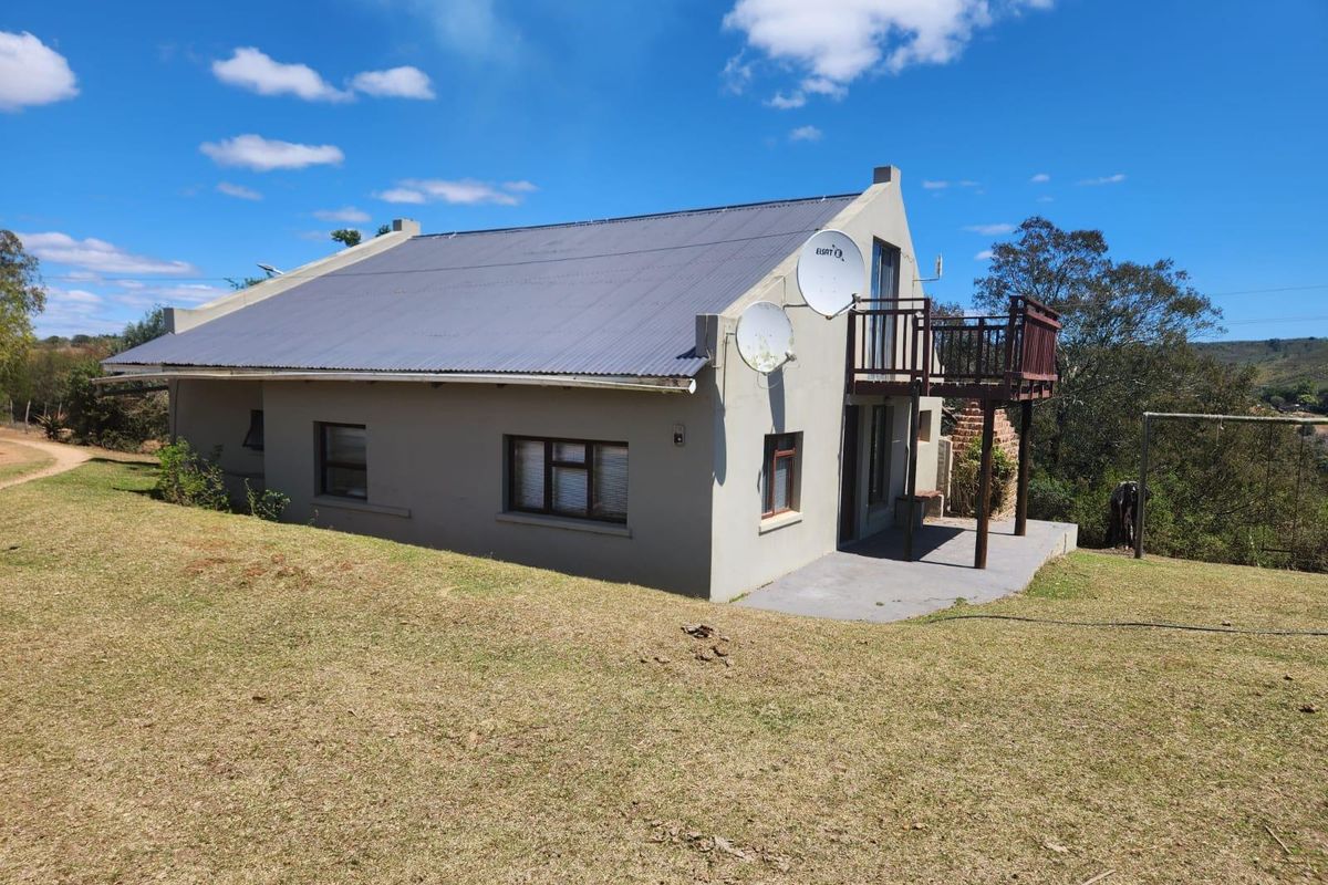 Rear view of the farm dwelling featuring a corrugated metal roof, a raised timber balcony, and a concrete patio area set within a grassy landscape.