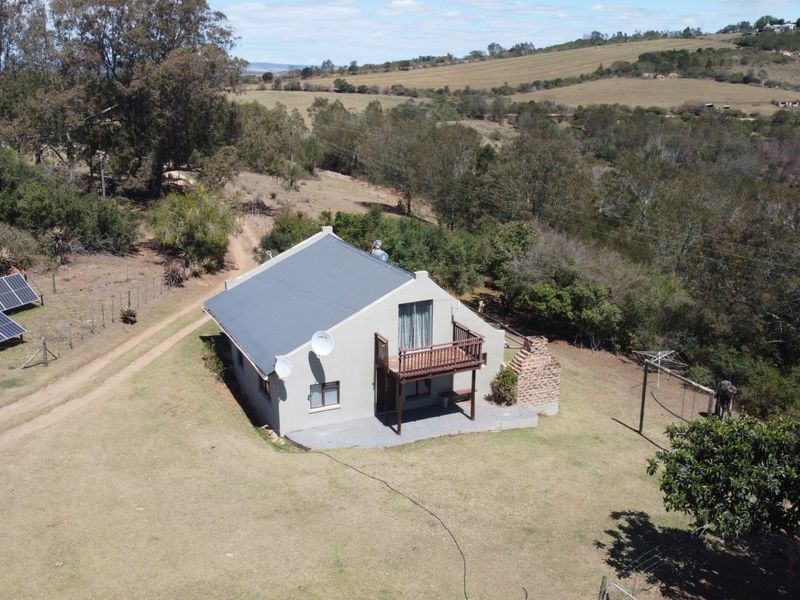 Aerial view of a rural farm property featuring a house with a metal roof, solar panels, a brick chimney, and a wooden balcony.